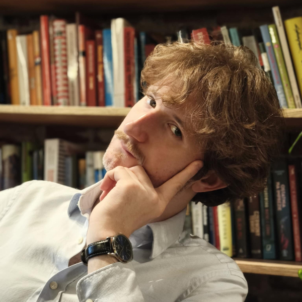 a man with his hand on his chin in front of a bookcase